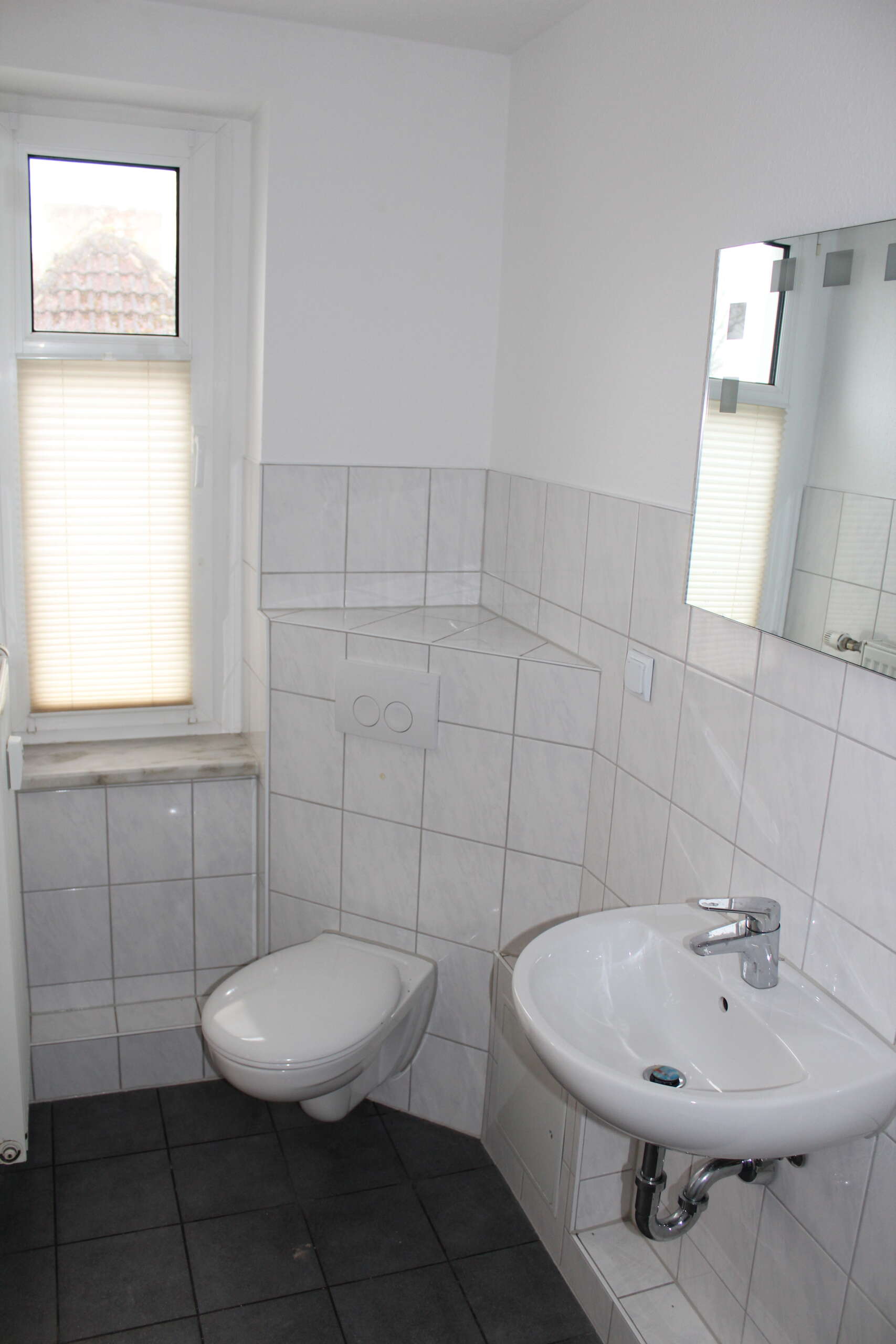 Modernes Badezimmer mit weiß gefliesten Wänden, Waschbecken und Toilette.