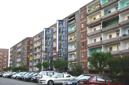 Reihen von Wohnblöcken mit bunter Fassade und geparkten Autos in einer Großstadtstraße.