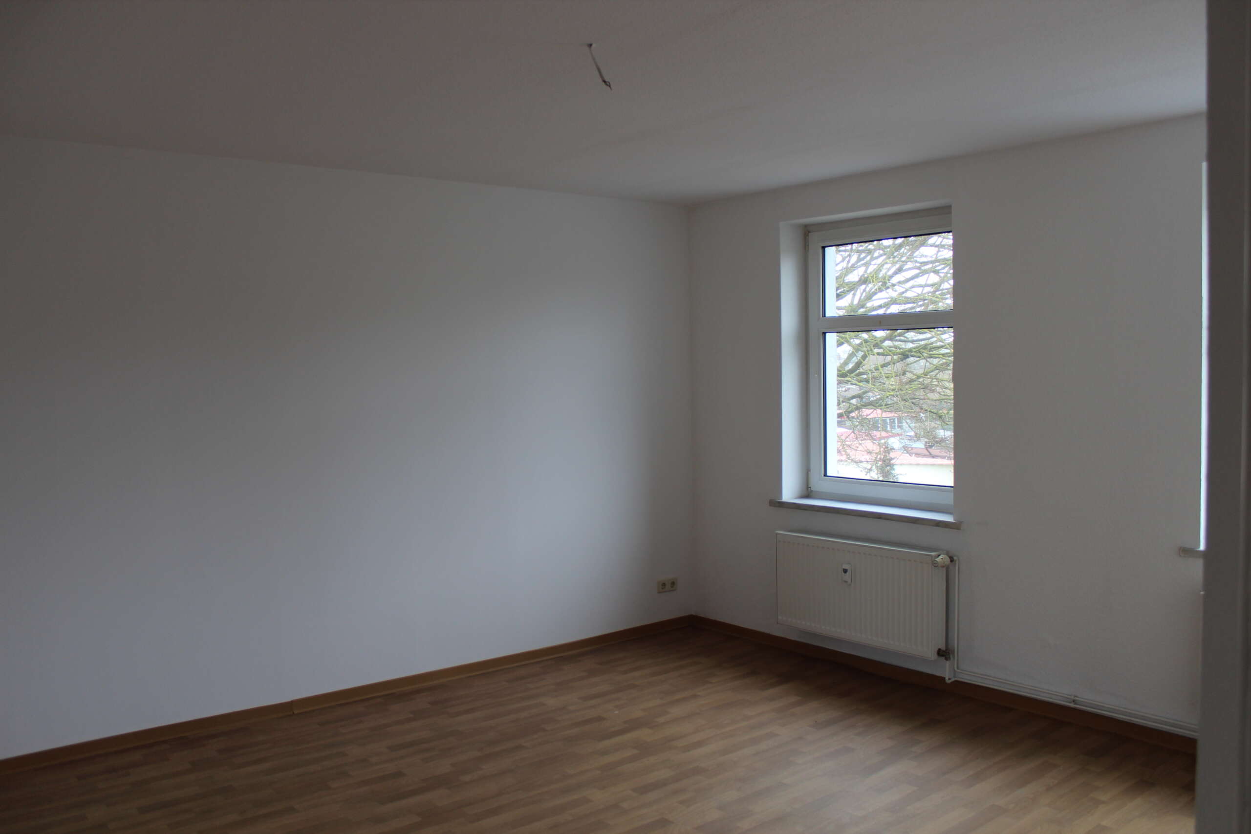 Leerer Raum mit weißer Wand, Fenster, Heizung und Holzfußboden, Blick ins Freie.