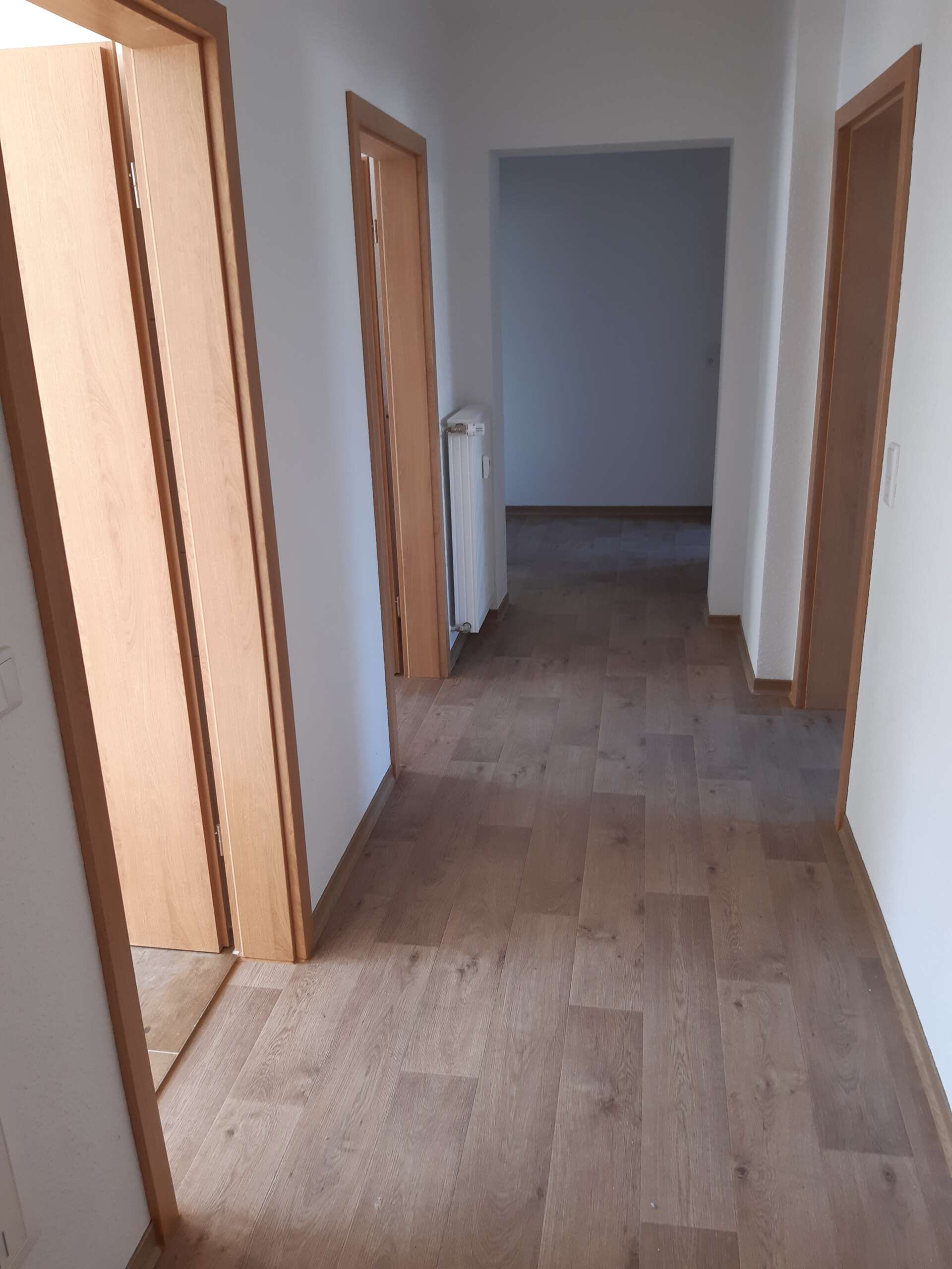Flur mit Holzboden, weißen Wänden und vier offenen Türen in einem Wohnraum.