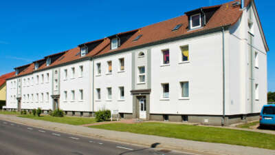 Weiße Mehrfamilienhäuser mit roten Dächern an einer Straße unter blauem Himmel.