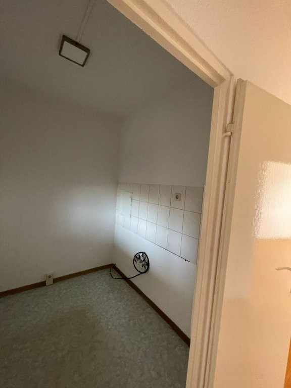 Leerer Raum mit gefliester Wand, Kabel auf dem Boden, Licht an der Decke, Tür im Vordergrund.