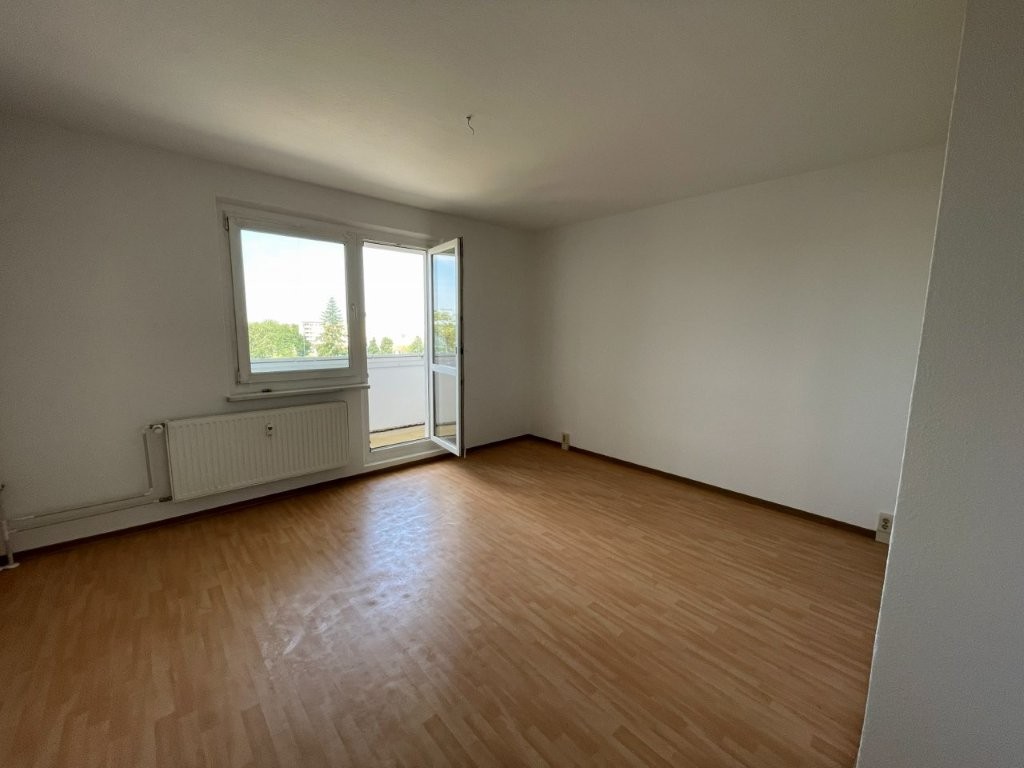 Leerer Raum mit Laminatboden, Fenster und offener Balkontür, viel Tageslicht.